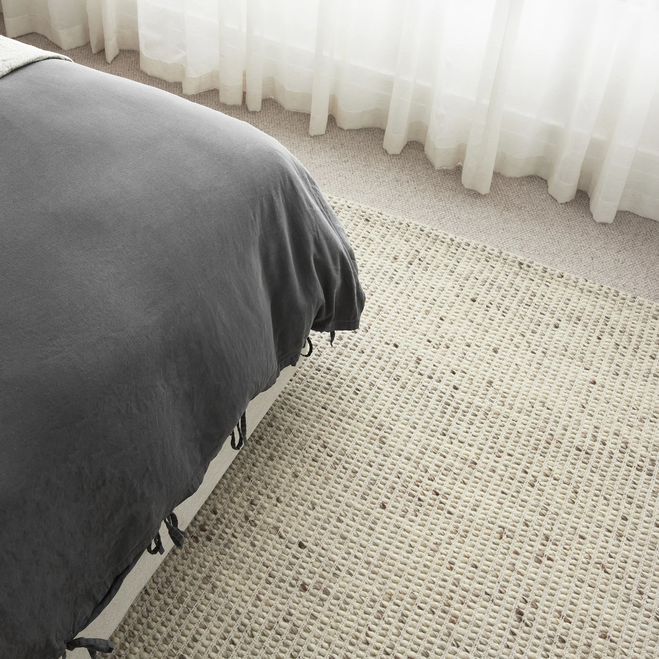 Elara Pebble wool rug beside a bed
